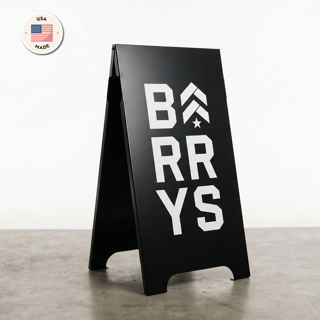 Black a-frame sign with 'BARRY'S' text on a gray floor and white wall background.