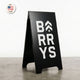 Black a-frame sign with 'BARRY'S' text on a gray floor and white wall background.