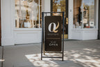 Outdoor sign for a boutique with 'Q' logo and 'We Are Open' text.