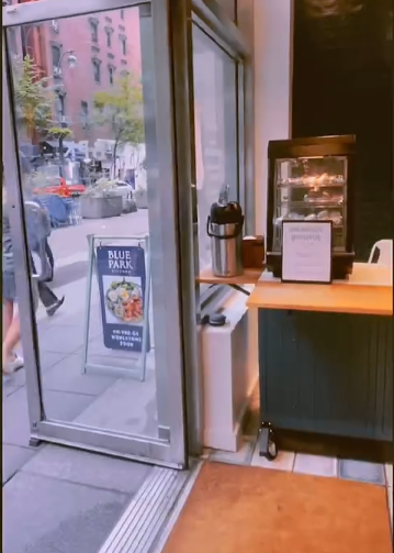 Entrance to a cafe with a glass door and a Blue Park sign on the sidewalk.