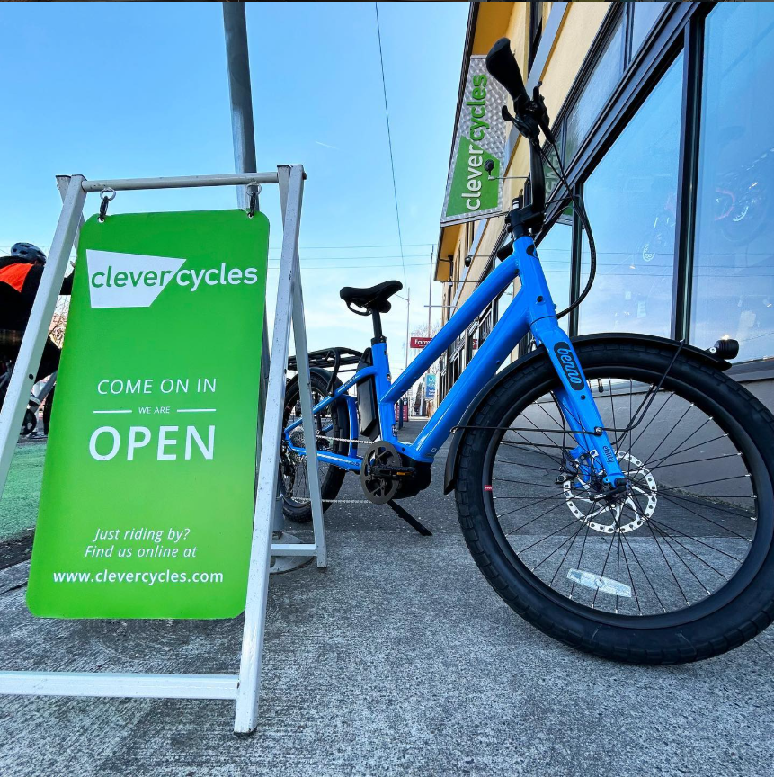 Blue bicycle parked next to a 'clevercycles' sign outside a store.