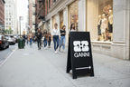 Ganni store sign on a city street with pedestrians walking by
