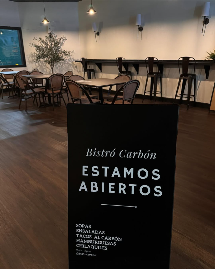 Restaurant interior with a sign indicating 'Bistró Carbón Estamos Abiertos' in a dining area.