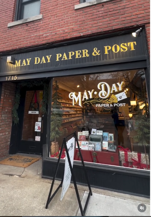 Storefront of May Day Paper & Post with a sign and display.