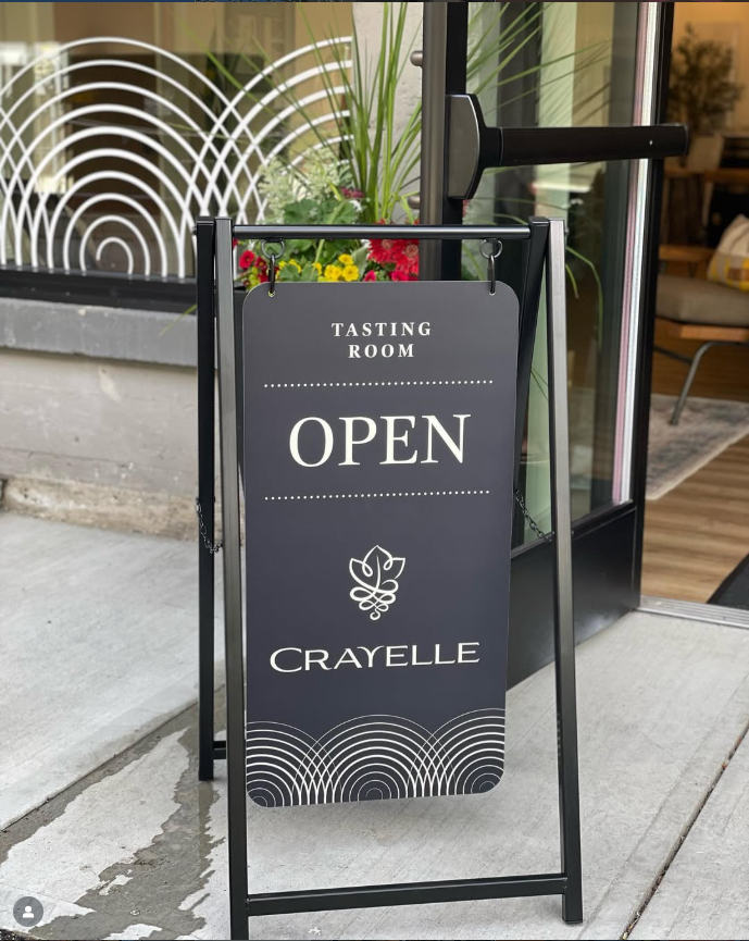 Open sign for Crayelle tasting room outside a building entrance.